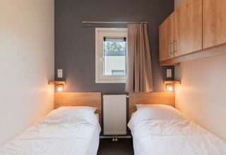 Dos camas individuales en una pequeña habitación acogedora con ventana, lámparas de pared y armarios en Beach lodge | Island, Vakantiepark Leukermeer.