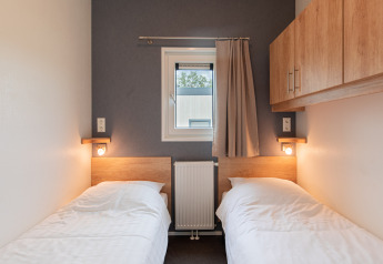 To enkeltsenge på et lille værelse med vindue, væglamper og skabe på Beach lodge | Island, Vakantiepark Leukermeer.