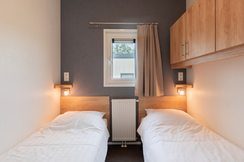 Dos camas individuales en una pequeña habitación acogedora con ventana, lámparas de pared y armarios en Beach lodge | Island, Vakantiepark Leukermeer.