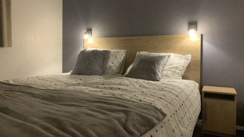 Dormitorio moderno con cama doble, mesita de noche y luces de pared en Beach Lodge, Vakantiepark Leukermeer.