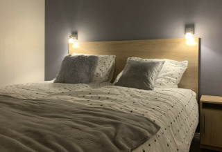 Dormitorio moderno con cama doble, mesita de noche y luces de pared en Beach Lodge, Vakantiepark Leukermeer.