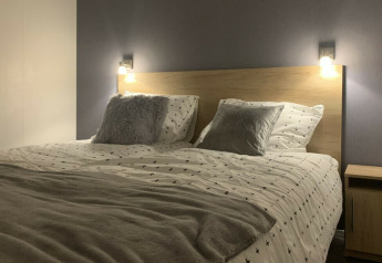 Dormitorio moderno con cama doble, mesita de noche y luces de pared en Beach Lodge, Vakantiepark Leukermeer.