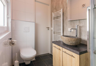 Moderne, kleine badkamer in Beach Lodge op Vakantiepark Leukermeer met stenen waskom en zwevend toilet.