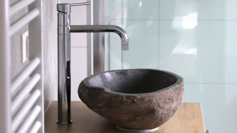 Moderno lavabo de baño con pila de piedra y grifo cromado en Beach lodge en Vakantiepark Leukermeer, Países Bajos.