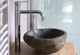 Moderno lavabo de baño con pila de piedra y grifo cromado en Beach lodge en Vakantiepark Leukermeer, Países Bajos.
