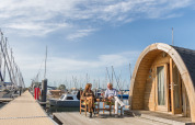 To personer sidder foran et tiny house ved Water bubbles, Marina Parcs Almere, omgivet af både.