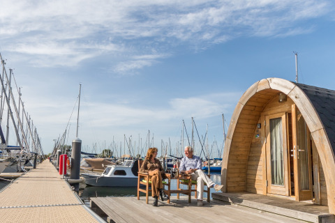 Deux personnes assises devant une tiny house Water bubbles à Marina Parcs Almere, entourées de bateaux.