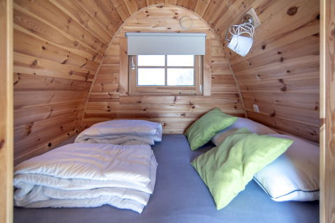 Pequeña casa de madera en Water bubbles, Marina Parcs Almere, con cama y almohadas verdes visibles.
