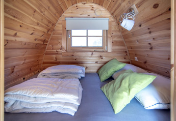 Pequeña casa de madera en Water bubbles, Marina Parcs Almere, con cama y almohadas verdes visibles.