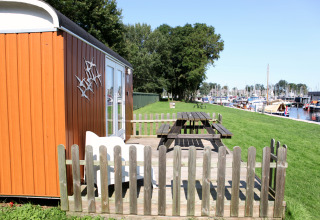 Kleine orange Hütte namens Tiny Wagons bei Marina Parcs Naarden, mit Garten und Blick auf den Hafen.