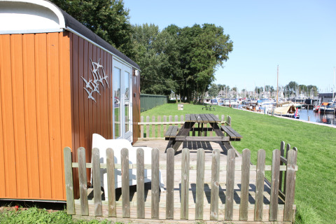Pequeña casa naranja llamada Tiny Wagons en Marina Parcs Naarden, con jardín y vista al puerto deportivo.