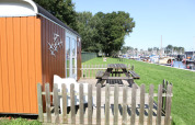 Pequeña casa naranja llamada Tiny Wagons en Marina Parcs Naarden, con jardín y vista al puerto deportivo.