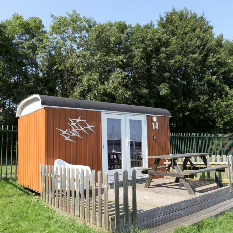Kleines Tiny House mit Holzterrasse und Sitzbank bei Marina Parcs Naarden, Niederlande, an sonnigem Tag.