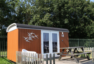 Lille hytte med terrasse og bord-bænkesæt ved Marina Parcs Naarden, Nederlandene, på solrig dag.