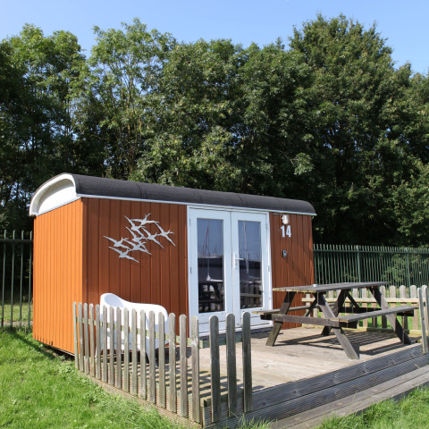 Lille hytte med terrasse og bord-bænkesæt ved Marina Parcs Naarden, Nederlandene, på solrig dag.