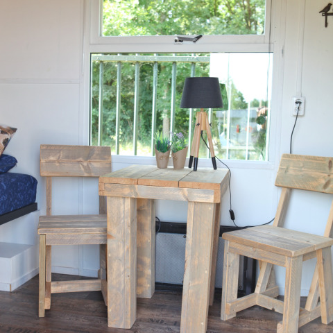 Træbord og stole ved et vindue i et Tiny House hos Marina Parcs Naarden, Holland, med udsigt til have.