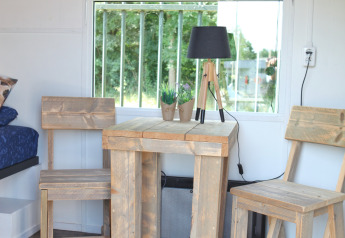 Træbord og stole ved et vindue i et Tiny House hos Marina Parcs Naarden, Holland, med udsigt til have.