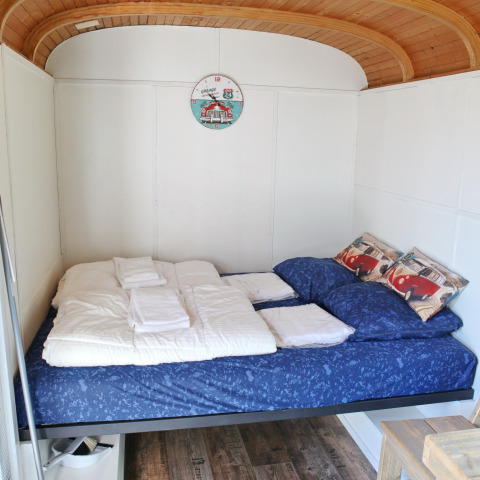 Cama acogedora con ropa azul y techo de madera en una tiny house en Marina Parcs Naarden, Países Bajos.