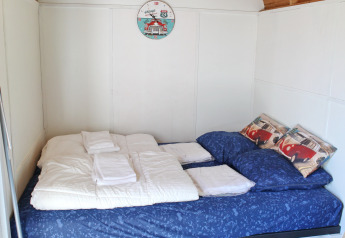 Cama acogedora con ropa azul y techo de madera en una tiny house en Marina Parcs Naarden, Países Bajos.