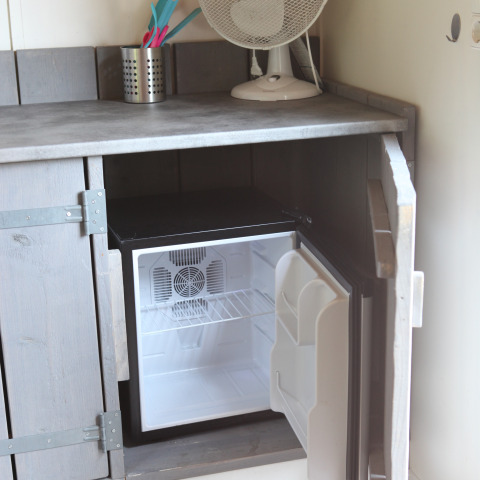 Una pequeña nevera minibar dentro de un armario bajo la encimera en una tiny house en Marina Parcs Naarden.