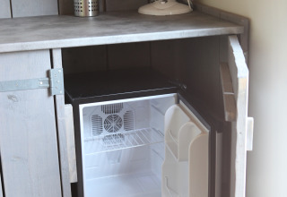 Een kleine minibar koelkast in een kast onder het werkblad in een tiny house bij Marina Parcs Naarden.