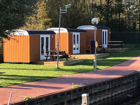 Tre små træhytter kaldet Tiny Wagons ved Marina Parcs Naarden i Holland, omgivet af grønne områder.