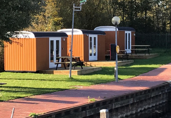 Tre små træhytter kaldet Tiny Wagons ved Marina Parcs Naarden i Holland, omgivet af grønne områder.
