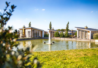 Moderne lodge Biebosch - Sunshower ved Resort Mooi Bemelen i Holland, med udsigt over en dam og fontæne.