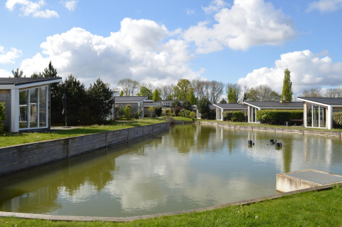 Moderne hytter ved en fredelig sø på Resort Mooi Bemelen i Holland under en skyet blå himmel.