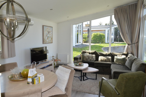 Helles Wohnzimmer in der Biebosch - Sunshower Lodge im Resort Mooi Bemelen, mit großer Couch und Gartenblick.