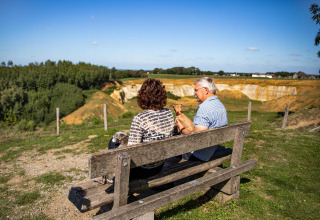 Couple âgé avec chien assis sur un banc, profitant de la vue à Biebosch - Sunshower, Resort Mooi Bemelen.