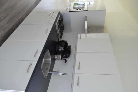 Moderne keuken met witte kasten, zwart werkblad, gootsteen, fornuis en toestellen in een vakantiehuisje.