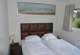 Slaapkamer met twee aparte bedden, bruin hoofdbord, lampen, raam en schilderij in Resort Mooi Bemelen.