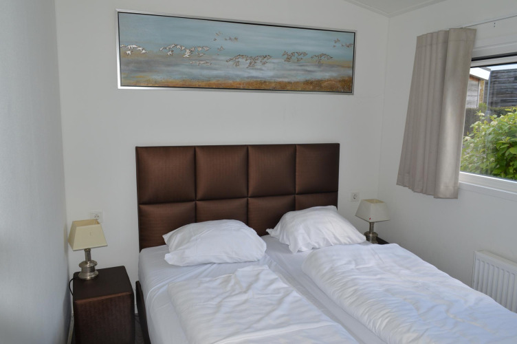 Bedroom with two beds, padded brown headboard, bird artwork, bedside lamps, and window at Resort Mooi Bemelen.