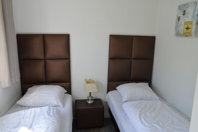 Room with two single beds, brown headboards, a nightstand, and wall art at Resort Mooi Bemelen in the Netherlands.