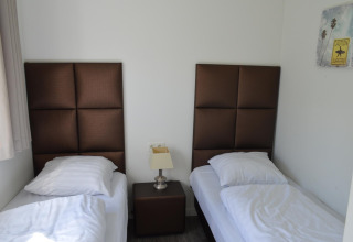 Kamer met twee eenpersoonsbedden, bruine hoofdborden, nachttafeltje en muurkunst in Resort Mooi Bemelen, Nederland.