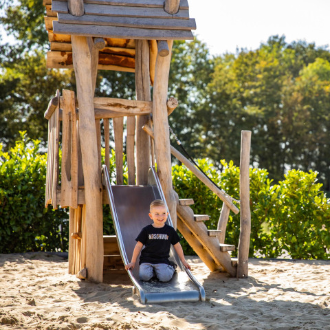 Niño jugando en un tobogán de madera en la cabaña Biebosch - Sunshower de Resort Mooi Bemelen, Países Bajos.