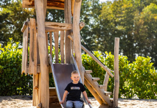 Niño jugando en un tobogán de madera en la cabaña Biebosch - Sunshower de Resort Mooi Bemelen, Países Bajos.