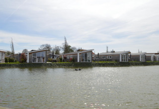 Lodges modernos junto al lago en Resort Mooi Bemelen, Países Bajos, vistos desde el agua en un día soleado.