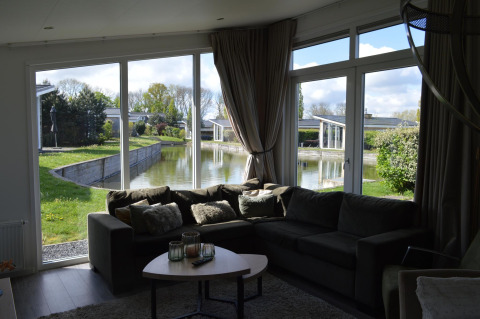 Sala de estar con sofá grande y mesa de centro, mostrando vistas de lago y jardines a través de amplias ventanas.