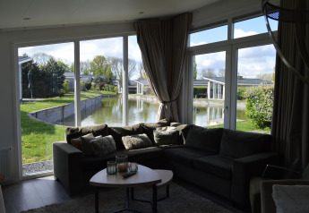 Sala de estar con sofá grande y mesa de centro, mostrando vistas de lago y jardines a través de amplias ventanas.