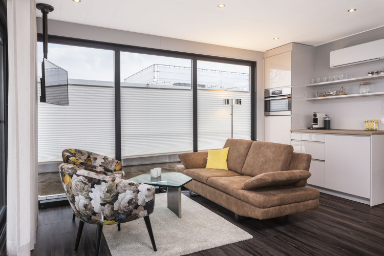 Salón moderno en una casa flotante en Offingawier, ventanales grandes, sofá marrón y sillones florales.