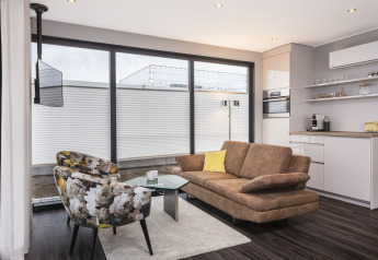 Salon moderne sur une péniche à Offingawier, grandes fenêtres, canapé brun et fauteuils fleuris.