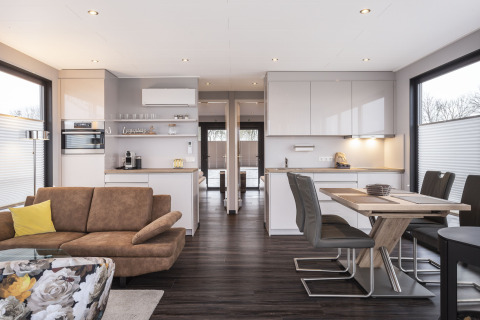 Sala y cocina modernas en una casa flotante con muebles de madera, grandes ventanas y mesa de comedor.