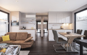 Modern living and kitchen area on a houseboat with wood furniture, large windows, and dining table.