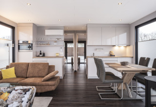 Sala y cocina modernas en una casa flotante con muebles de madera, grandes ventanas y mesa de comedor.