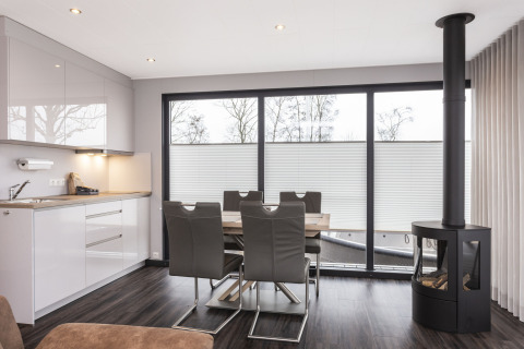 Modern houseboat with kitchen, dining area, and stove, large windows offering views in Offingawier, Netherlands.