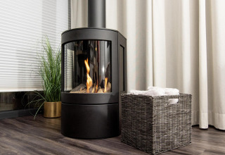Chimenea moderna junto a una cesta de mimbre y planta verde en casa flotante con cortinas y suelo de madera.