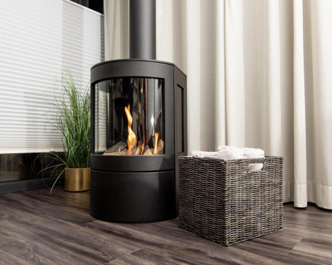 Modern fireplace next to a wicker basket and a green plant on a houseboat with curtains and wood flooring.