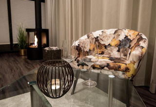 Salon d’une péniche à Offingawier avec fauteuil fleuri, table en verre, verres à vin et cheminée.
